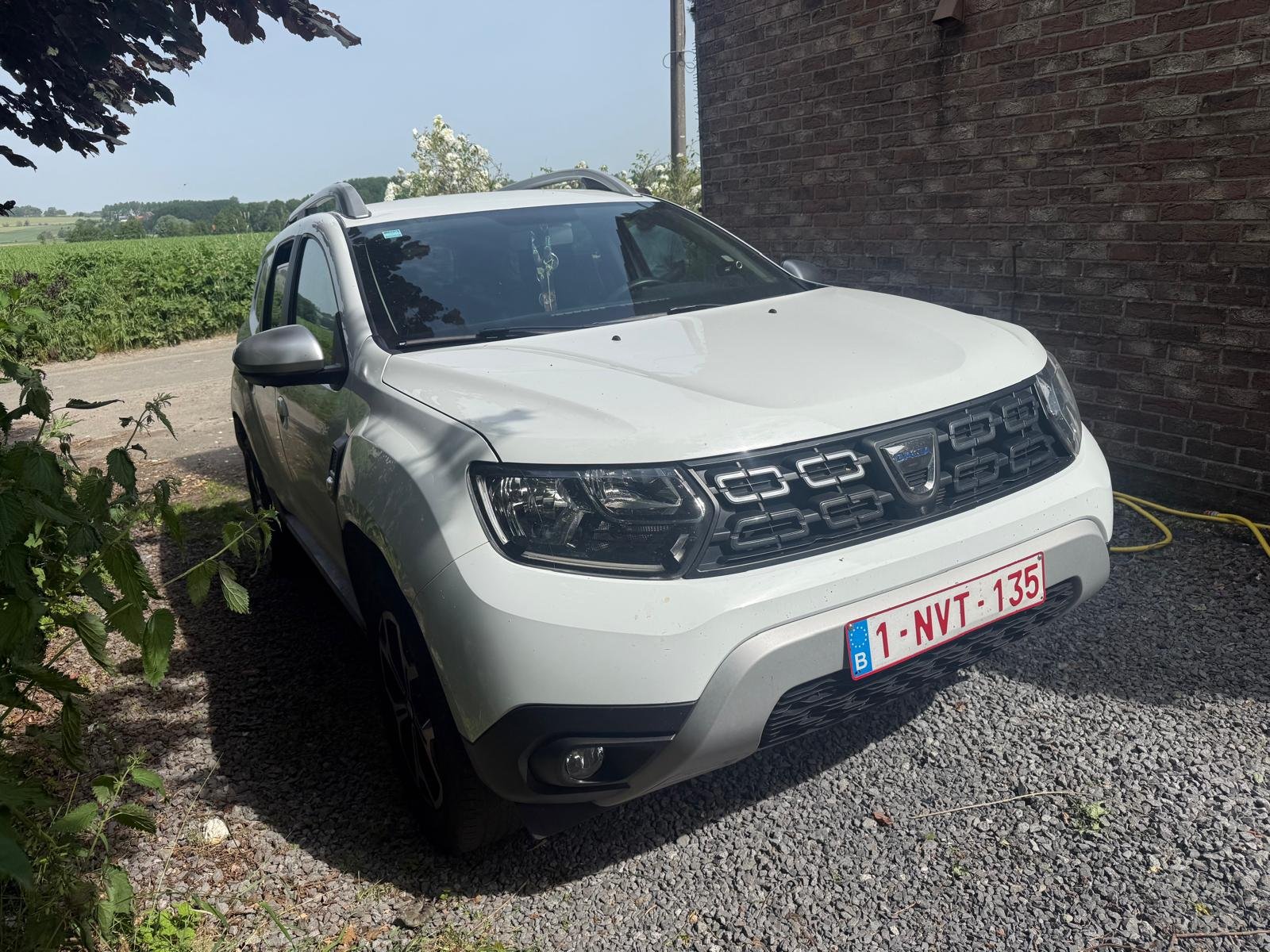Witte Dacia Duster naast een bakstenen muur in Izegem