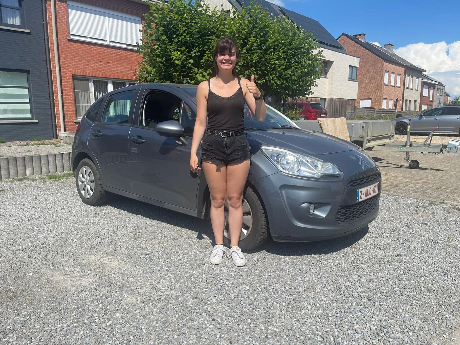 Vrouw met opgestoken duim naast een grijze Citroën C3 in Gavere