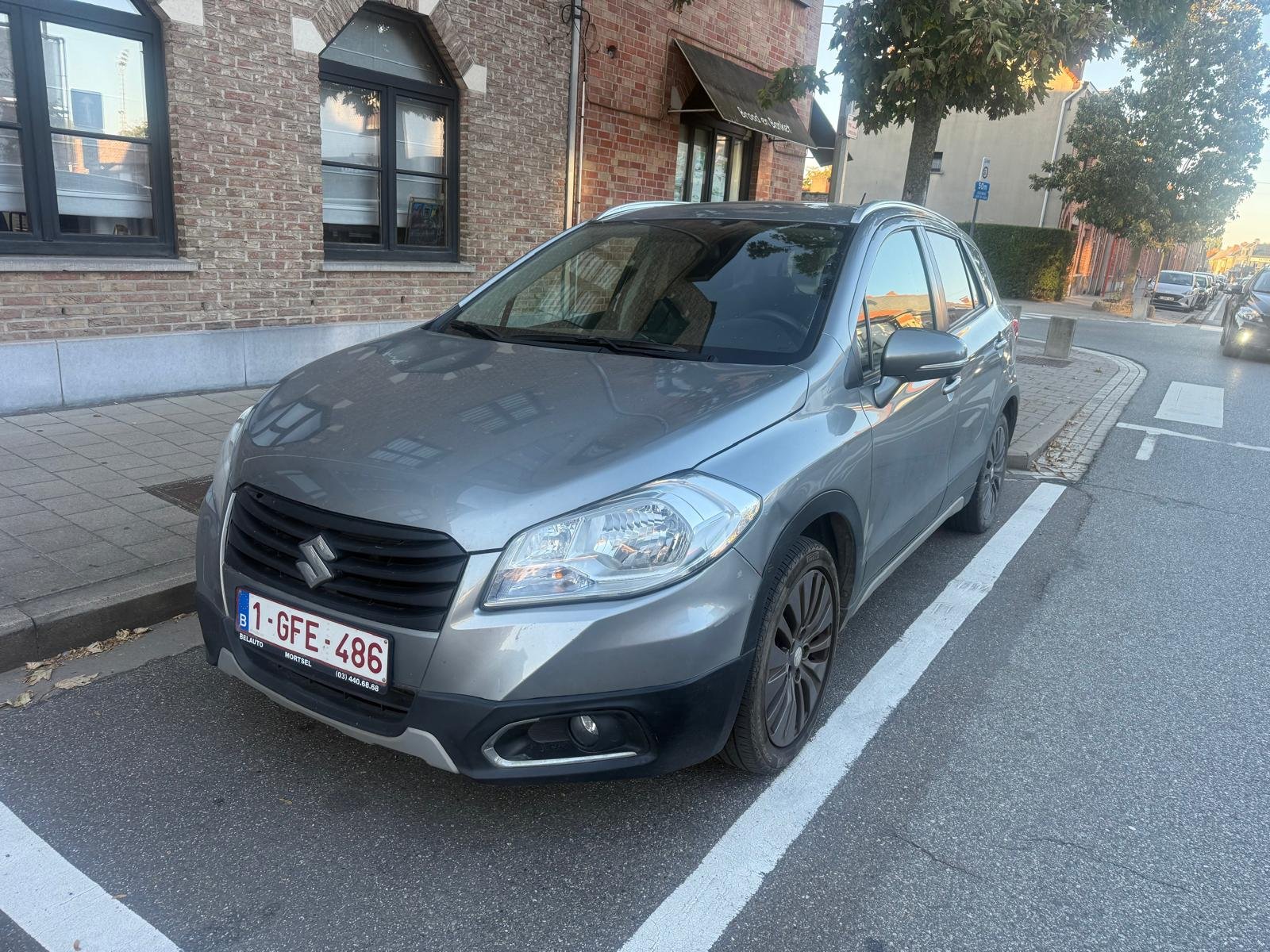 Grijze Suzuki SX4 uit 2016 geparkeerd langs een straat