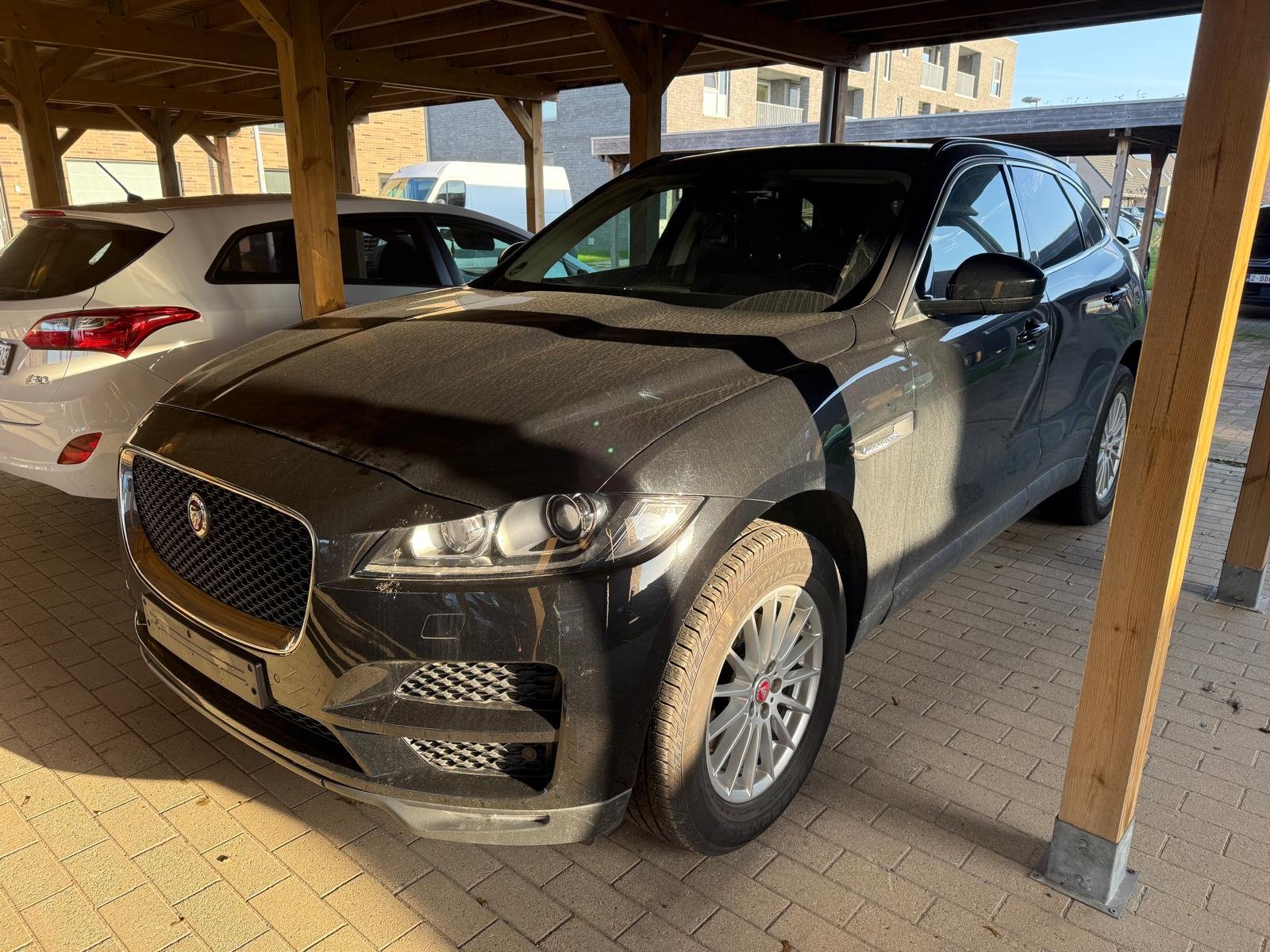 Donkere Jaguar F-Pace uit 2017 onder een houten carport